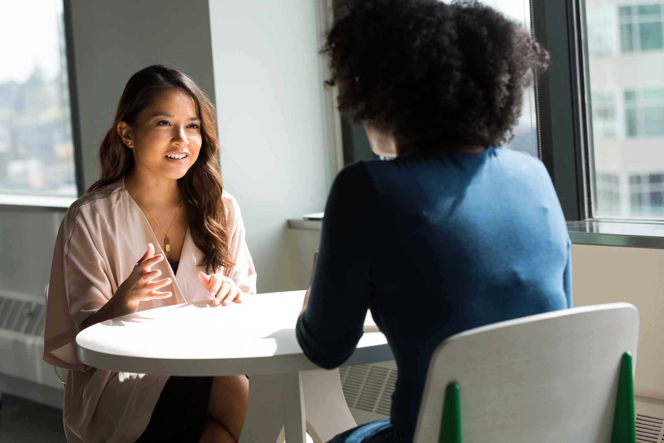 Two women sitting at talking at a table. One woman is talking with her hands.